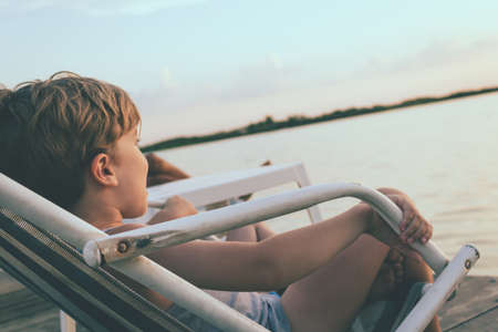 Small boy relaxing on a pier at sunset.の写真素材
