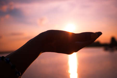 Hand holding sun above the sea. Summer sunset in hand of a woman.