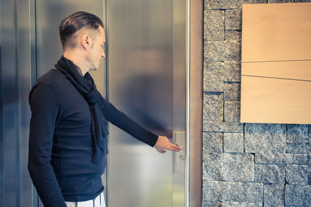 Man pressing elevator butting in a building hallway.の写真素材