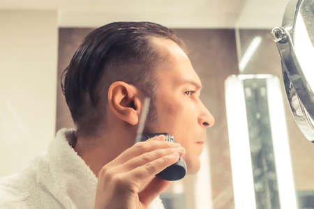 Close-up of man shaving with electric razor.の写真素材
