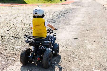 Rear view of boy driving quadbike on extreme terrain.の写真素材