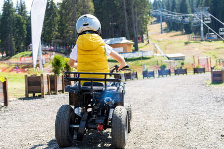 Rear view of kid driving quadbike on dirt road.の写真素材