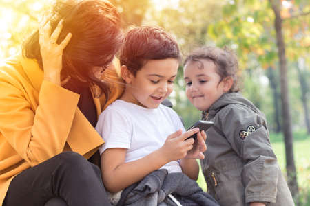 Happy boy looking something on cell phone with his mother and sister in the park.の写真素材