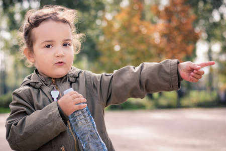 Little girl pointing at something in the distance while holding bottle of water in the park.の写真素材