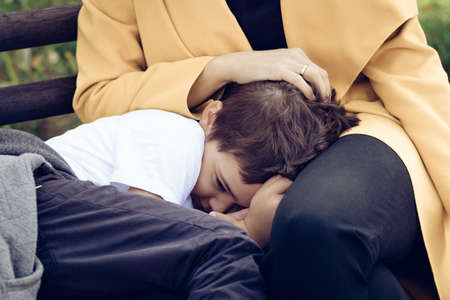 Sad son comforting in mother's lap. Shy little boy hiding in mother's embrace.