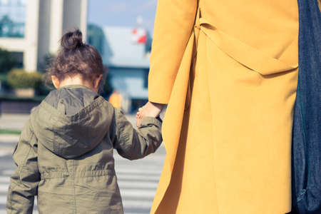 Rear view of daughter holding mother's hand while crossing the street.の写真素材