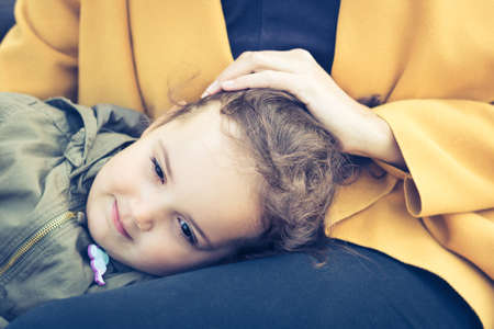 Cute thoughtful girl resting on mothers lap and day dreaming. Pensive daughter seeking shelter in mother's lap.の写真素材
