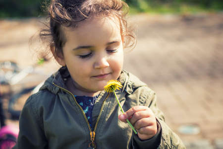 Small girl smelling dandelion with eyes closed. Cute little girl enjoying in pleasant smell of a flower.の写真素材