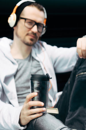 Close-up of man with headphones drinking takeaway coffee outdoors.