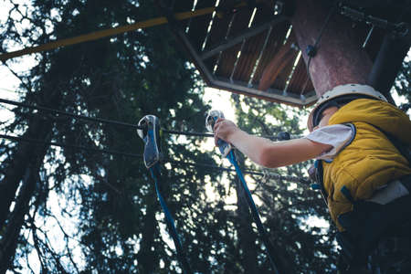 Low angle view of small boy attaching carabiner on a rope during canopy tour in adventure park.