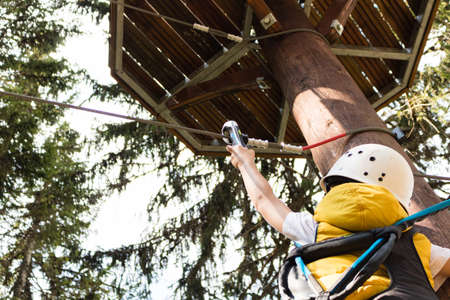 Low angle view of child attaching carabiner to zip line on canopy tour in the forest.