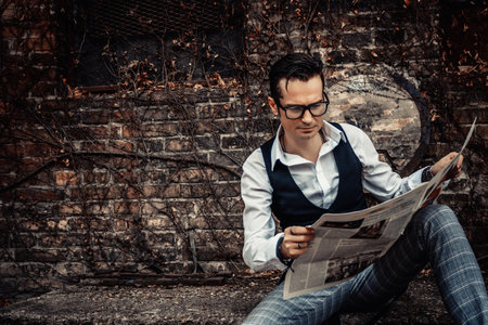 Retro-styled man reading newspaper while relaxing outdoors.の写真素材
