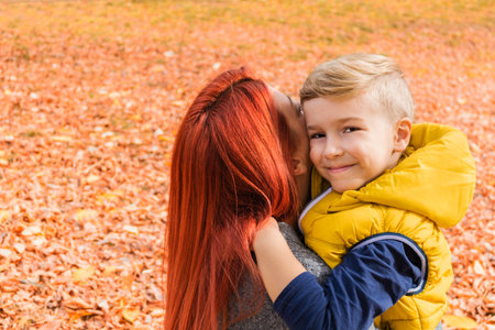 Happy kid embracing his mother during an autumn day at the park.の写真素材