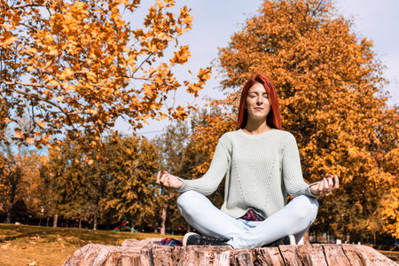 Zen-like woman practicing Yoga in lotus position and meditating with eyes closed in autumn day at the park.の写真素材
