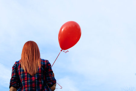 Back view of girl holding red balloon against the sky. Copy space.の写真素材