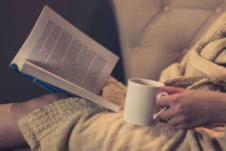 Close up of woman drinking tea and reading a book at night at home.の写真素材