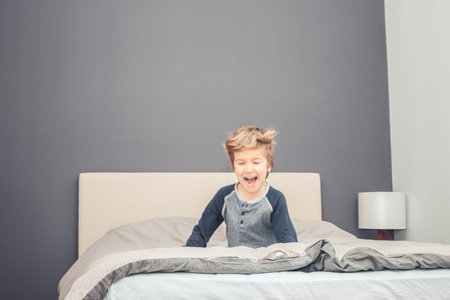 Happy little boy laughing while playing on the bed in the evening.の写真素材