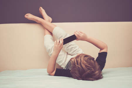 Kid relaxing watching cartoons on the internet while relaxing on the bed.の写真素材