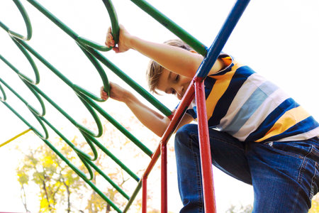 Happy boy climbing while playing on the playground in nature.の写真素材