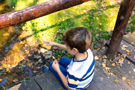 High angle view of a boy relaxing on wooden bridge above the creek in nature.の写真素材