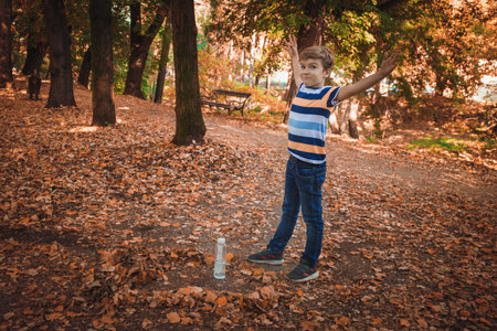 Happy kid standing with arms outstretched while making bottle flip in nature.の写真素材