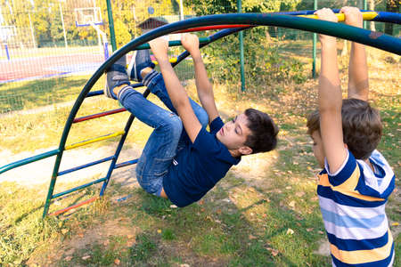 Playful boys having fun with monkey bars at the playground in nature.