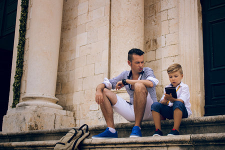 Father and son sitting on steps while relaxing in the city. Small boy and his father while relaxing on staircase in old town.の写真素材