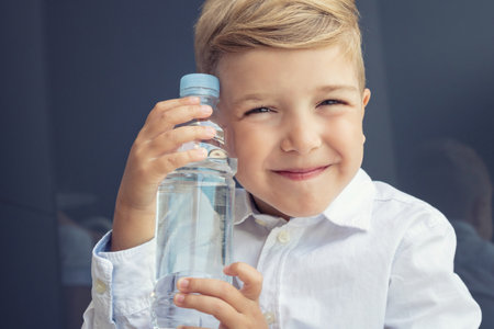 Little bot holding water bottle and smiling towards the camera. Photo of cute kid with water bottle.の写真素材