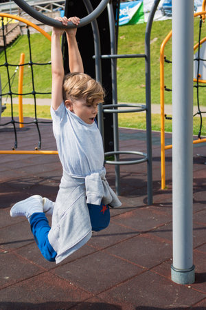 Little boy having fun while playing on the playground and hanging on a bar.