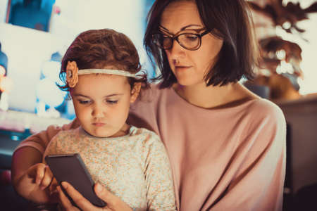 Mother and daughter using mobile phone while spending time together at home.の写真素材