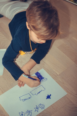 creative boy lying on the floor and sketching on a piece of paper.