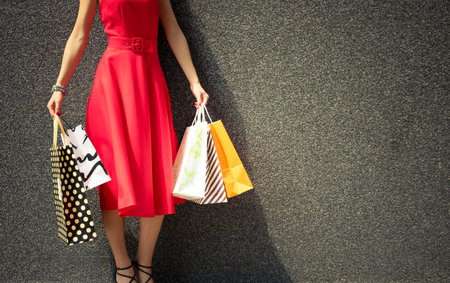 Unrecognizable woman in red dress holding shopping bags. Elegant woman after shopping day against the wall.の写真素材