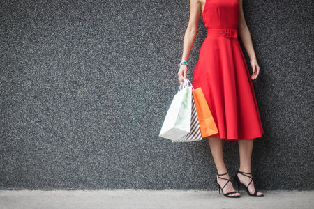 Unrecognizable woman in red dress holding shopping bags. Elegant woman after shopping day against the wall.  copy space.の写真素材
