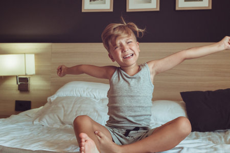 Cute kid stretching on the bed while waking up in the morning.の写真素材