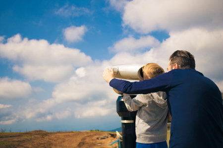 Rear view of father and son looking through telescope and exploring the nature. Copy space.