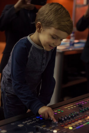 Happy boy adjusting sound on audio mixer in music studio.