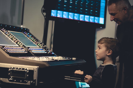 Small boy adjusting sound on audio mixing panel with help of music editor in recording studio.の写真素材