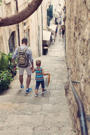 Father and son holding hands while walking through old tow on their summer vacation.の写真素材