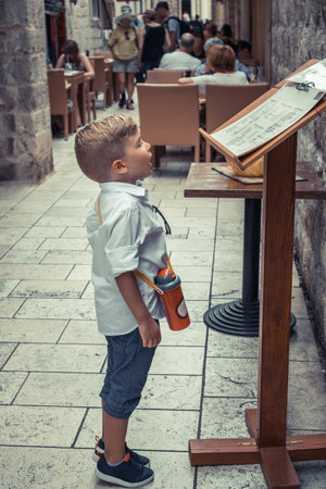 Small boy reading restaurant menu while standing on the street during summer vacation.の写真素材