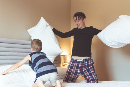 Playful father and son playing with pillows and having fun in bedroom.の写真素材