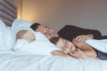 Small boy and his father sleeping together on the bed.の写真素材