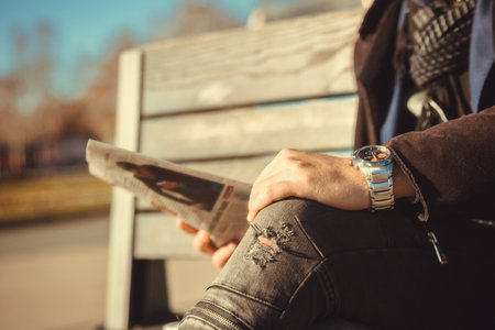 Close up of man reading daily newspaper while relaxing on a bench in the city.