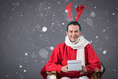 Happy man with reindeer antlers holding gift box and enjoying in New Year's holidays with snowflakes around him.の写真素材