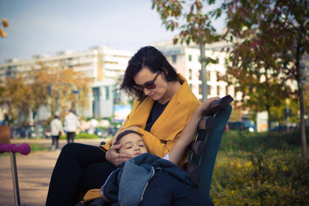 Little boy relaxing on mother's lap while spending a day together in the park. Affectionate mother consoling her son.の写真素材