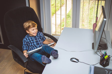 Happy little boy having fun while using computer at home.