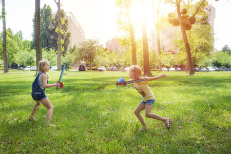 Happy small girls having fun and playing with pirate swords in the park.の写真素材