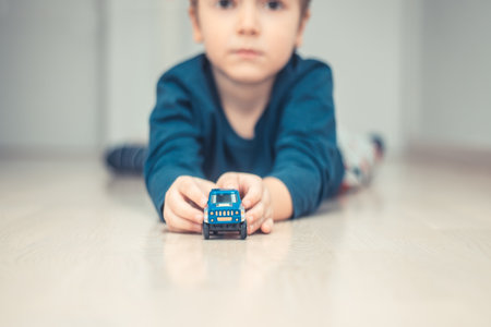 Small kid holding toy car while lying on the floor and playing at home.の写真素材