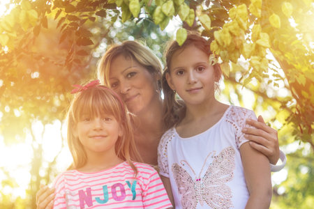 Portrait of happy mother embracing her two daughters in the park.の写真素材