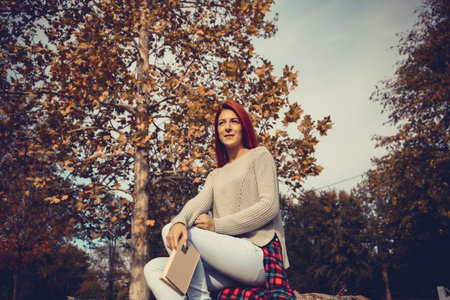 Young red-haired woman with a book relaxing in nature and thinking about something.の写真素材