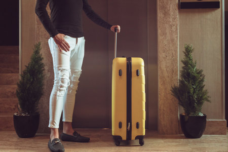 Unrecognizable man with suitcase waiting for elevator while standing in hotel lobby.の写真素材